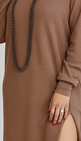 Brown ribbed dress with a black beaded necklace and a hand wearing a ring.