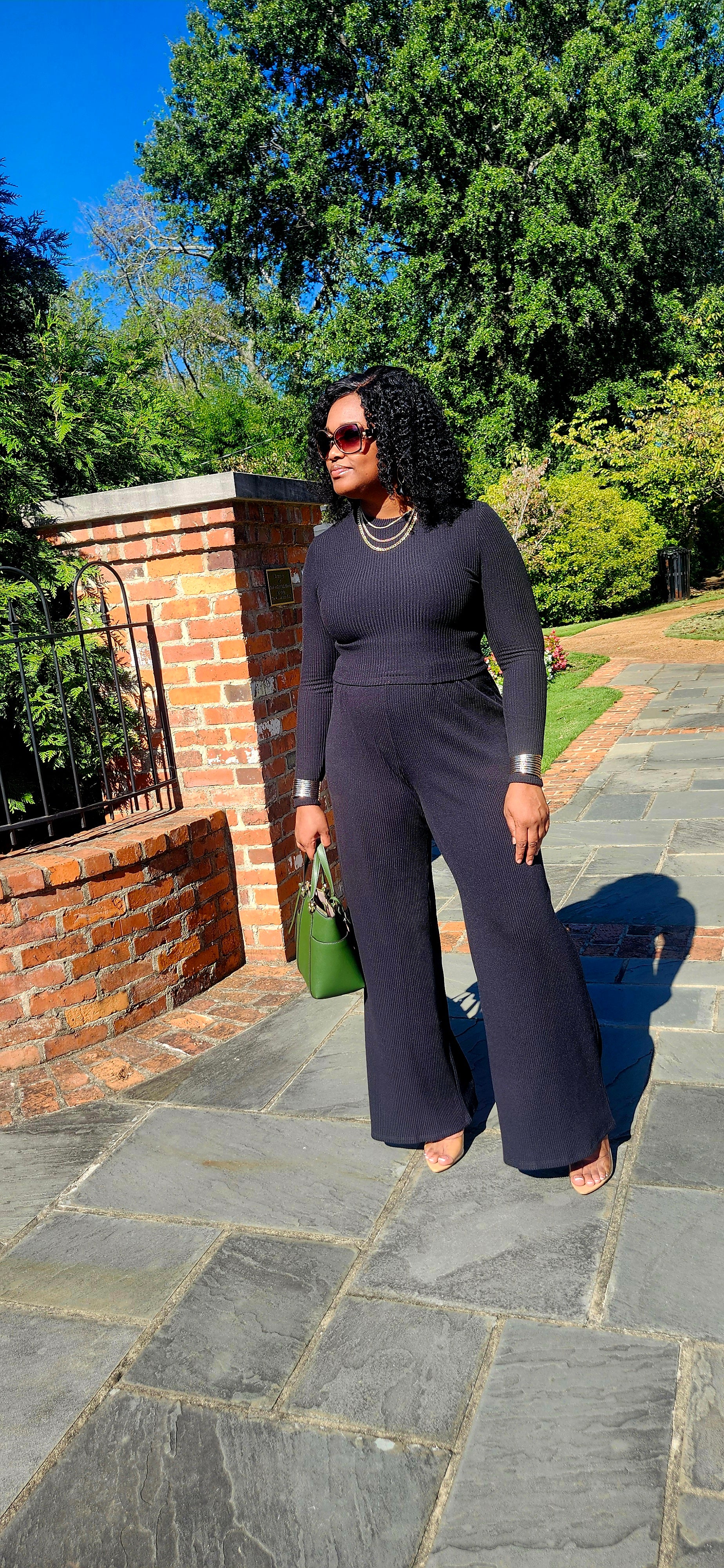 Woman in a black outfit standing outdoors on a stone path with trees in the background