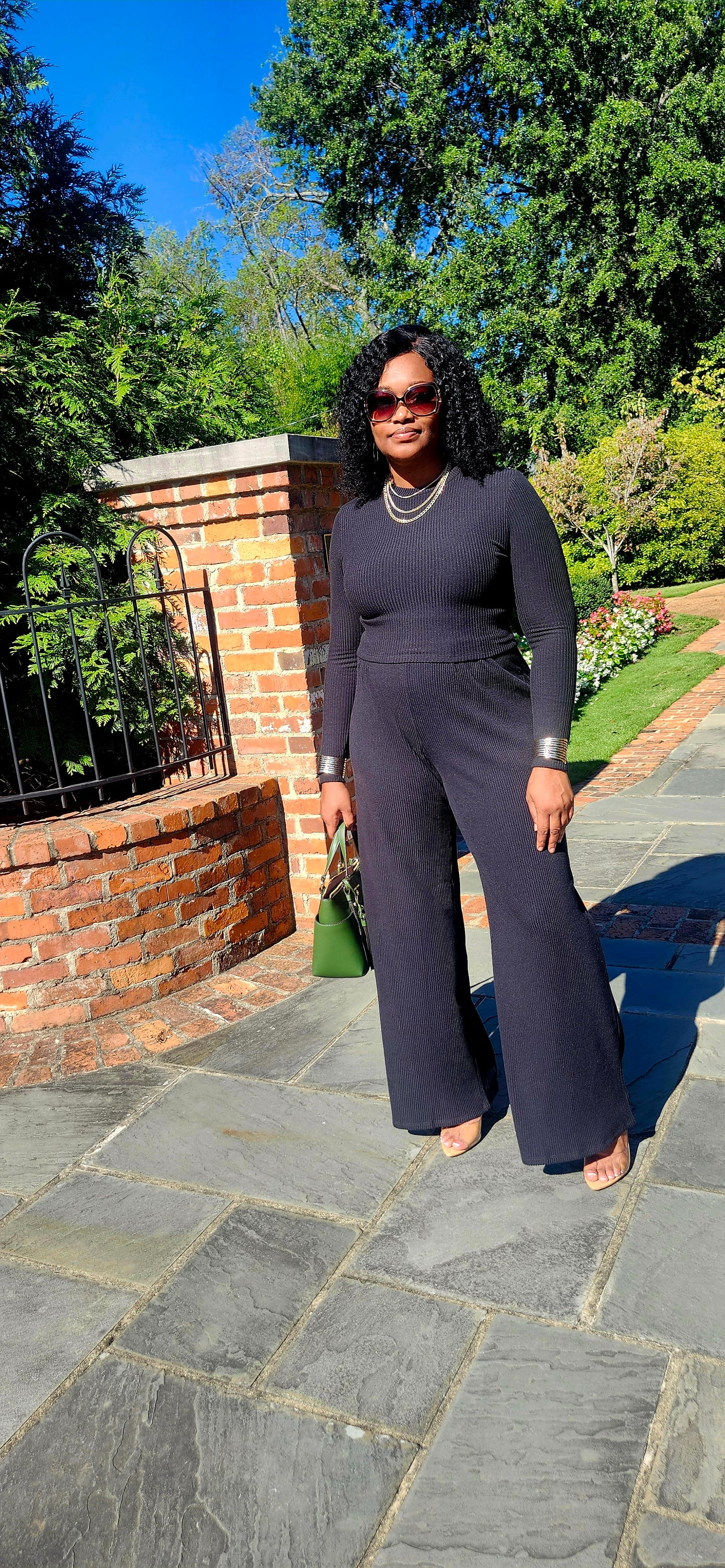 Woman in a navy outfit standing on a stone path with trees and a brick wall in the background