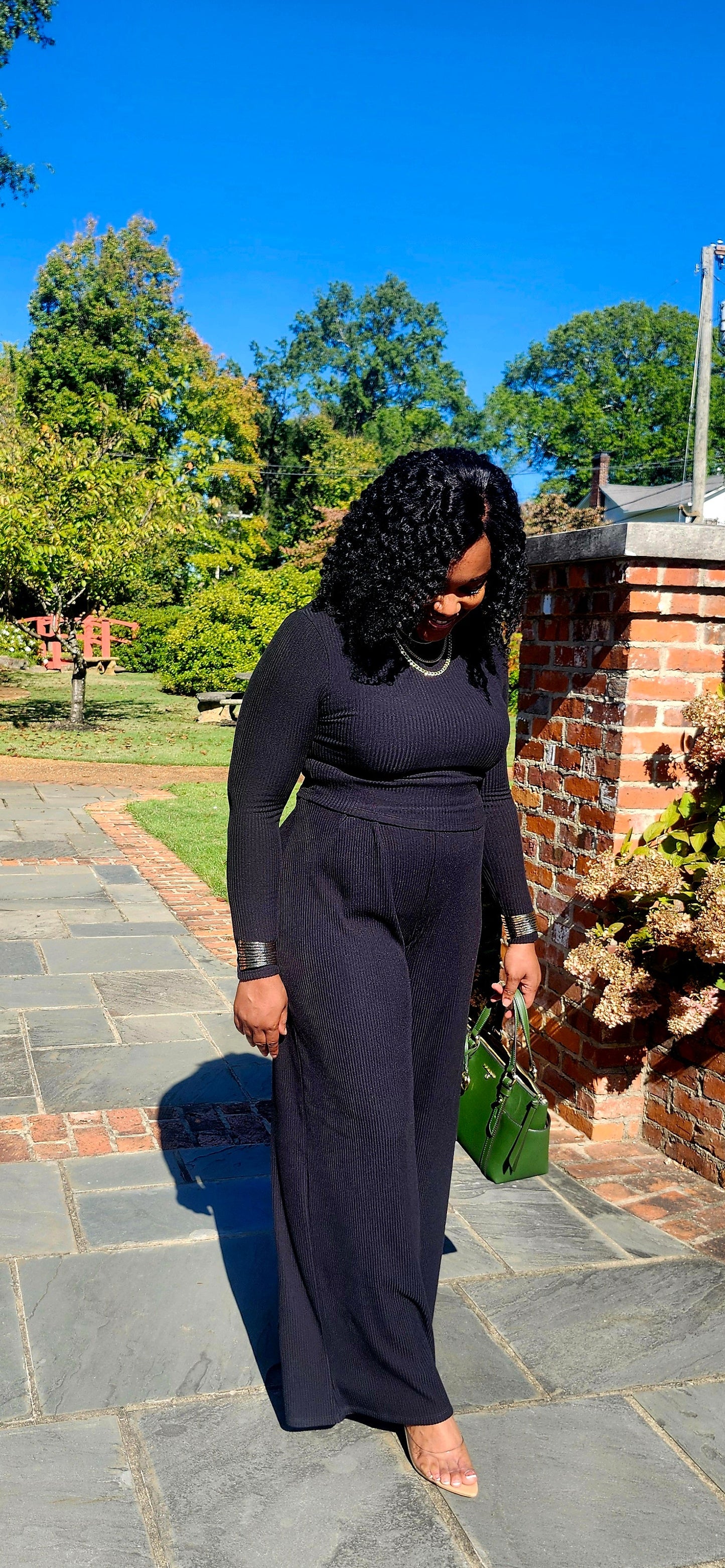 Woman in a black outfit walking outdoors with a suitcase.