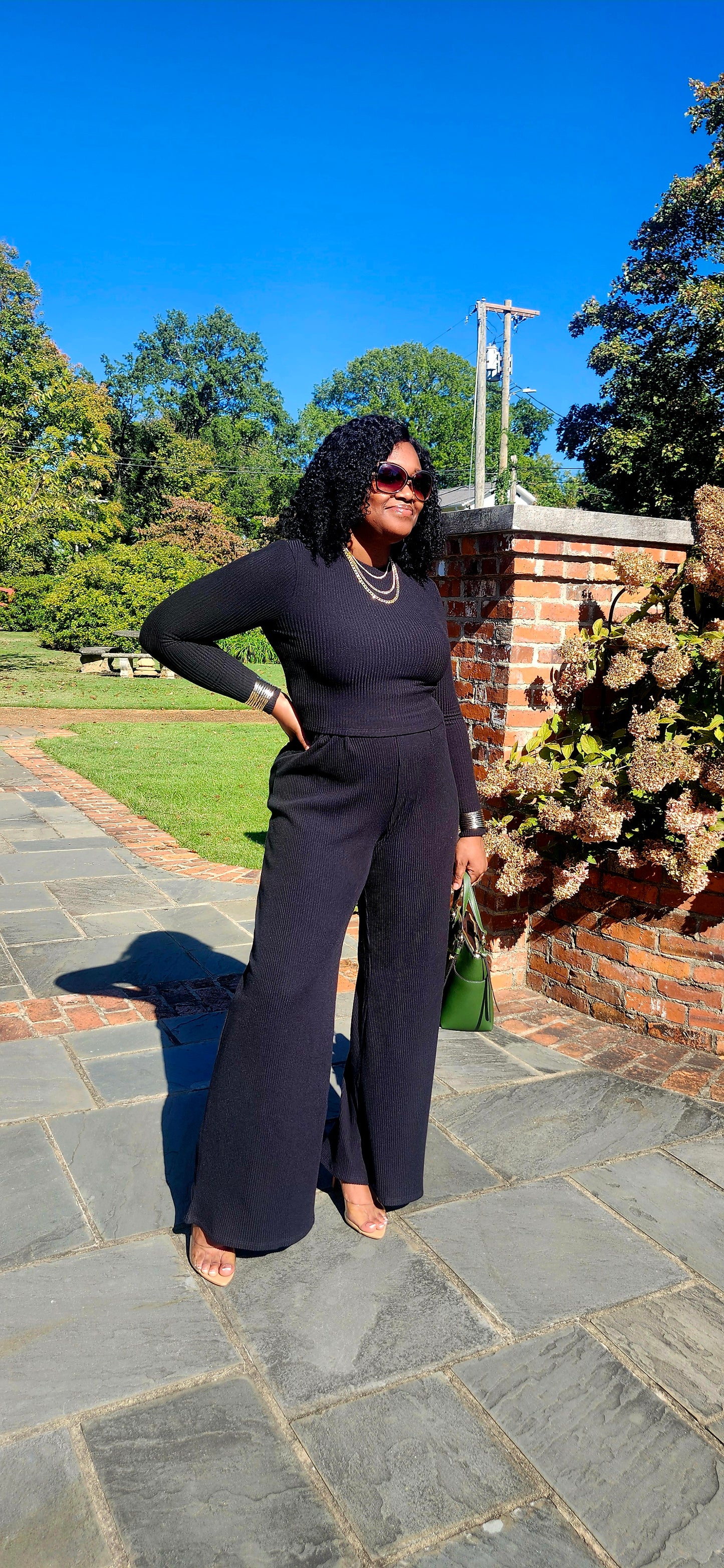 Woman in a black outfit standing on a stone path with greenery in the background