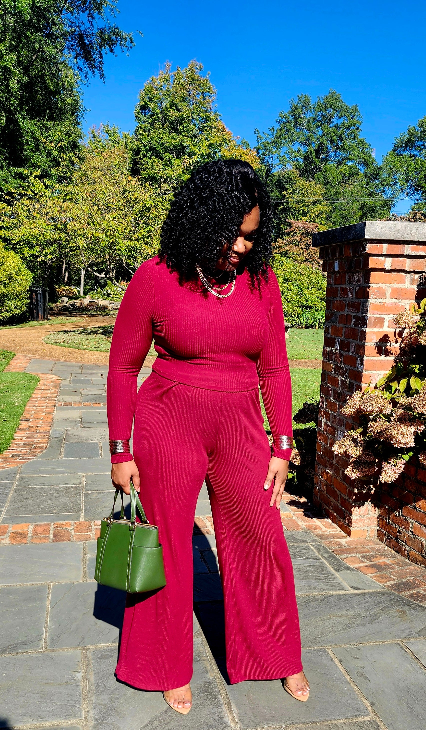 Woman in a red outfit standing outdoors on a stone path with trees in the background