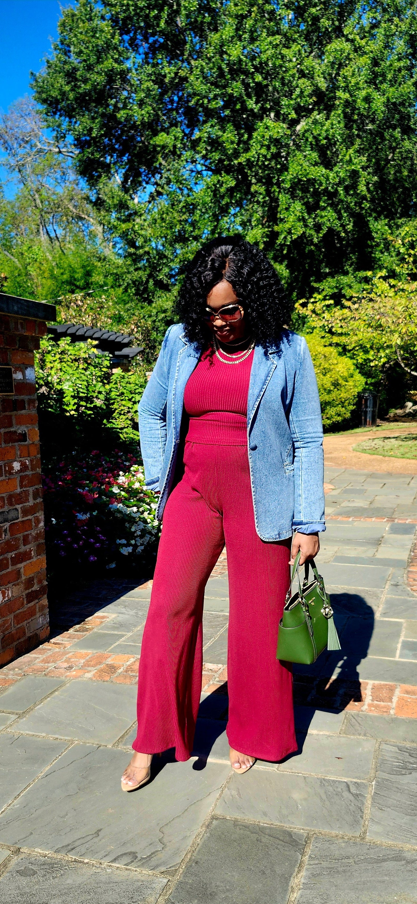 Woman in a pink dress and blue blazer standing on a stone path with greenery in the background