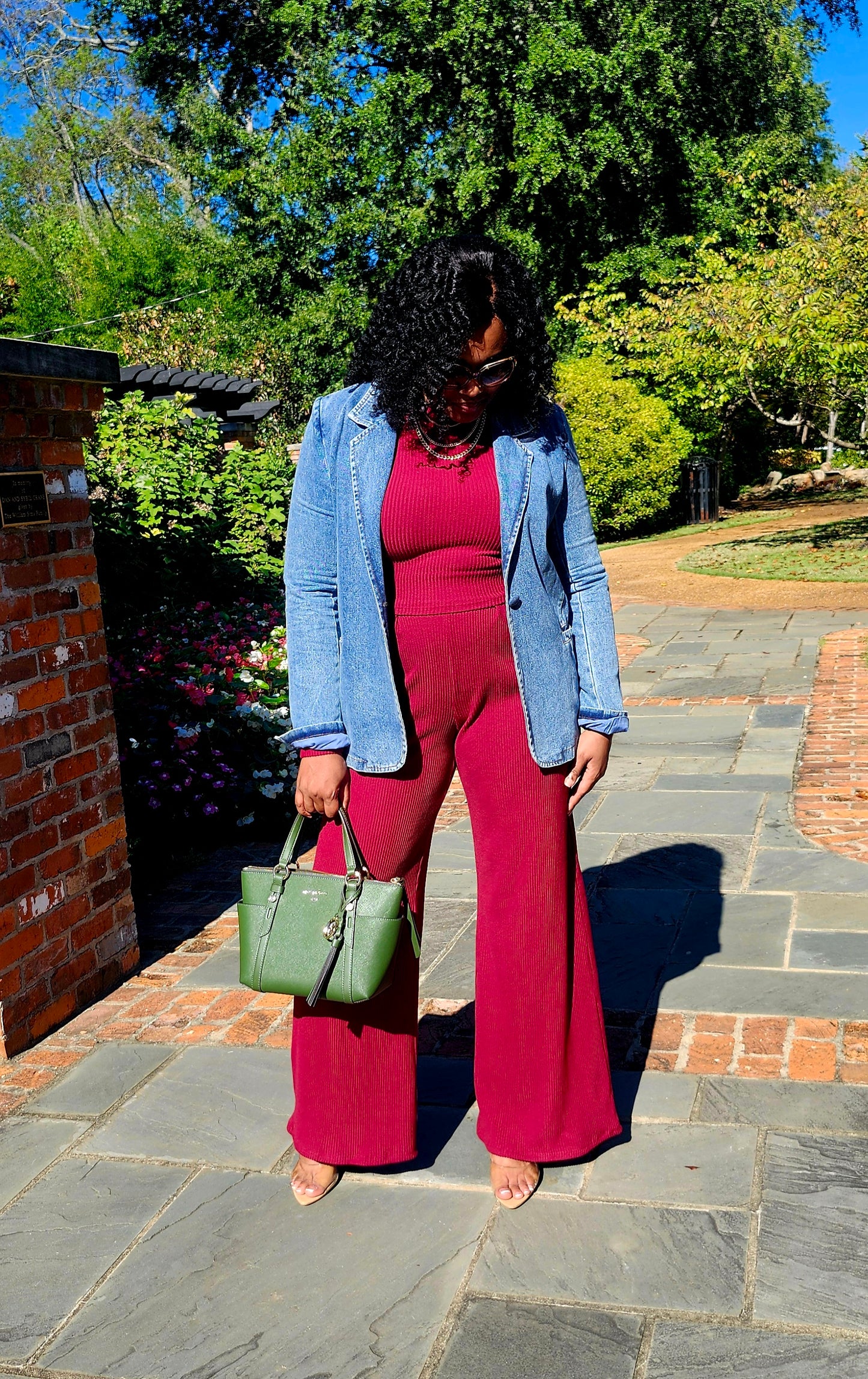 Woman in a pink outfit with a denim jacket and green handbag standing outdoors.