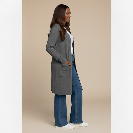 Woman wearing a gray cardigan, white shirt, blue jeans, and white sneakers on a beige background