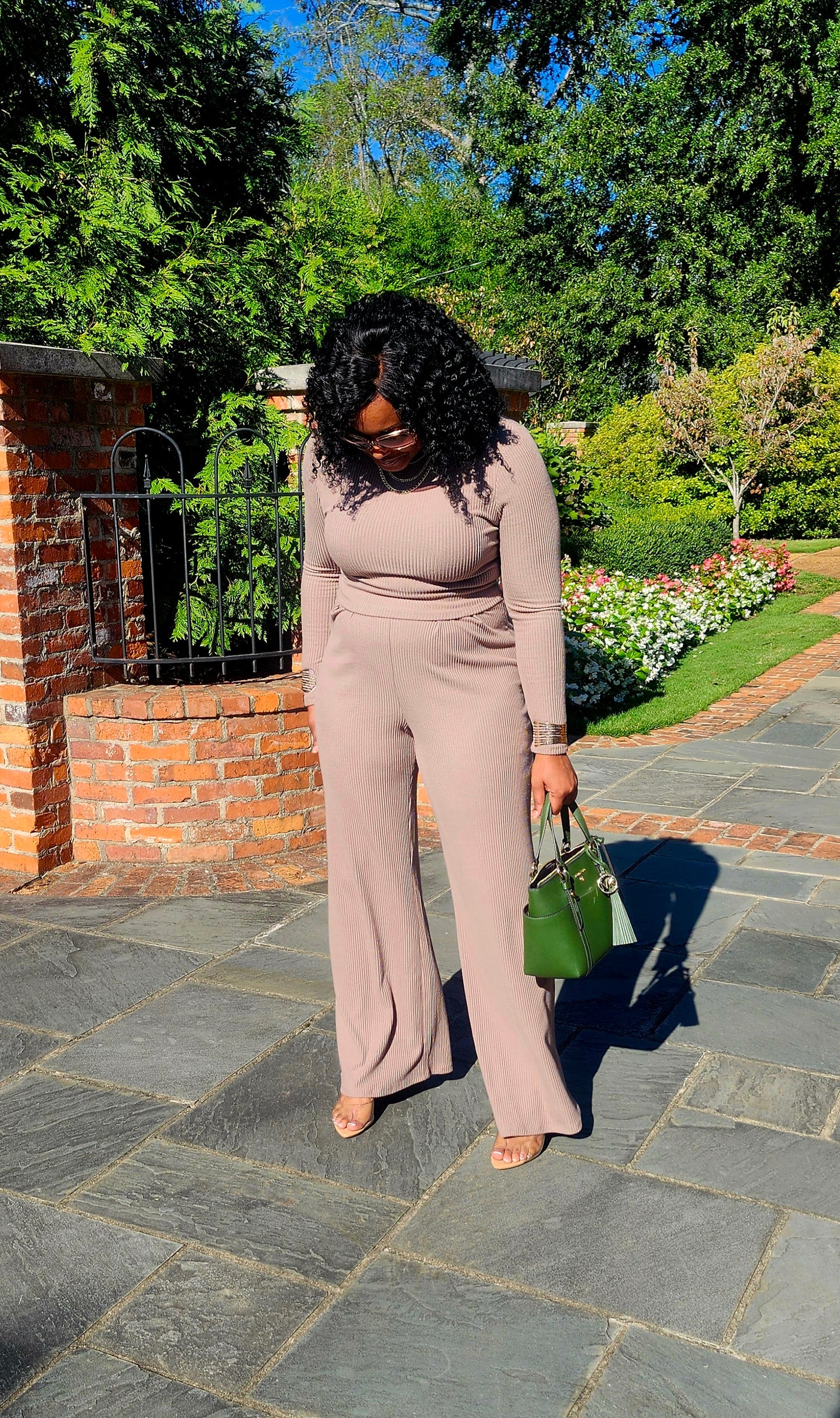 Woman in a beige outfit standing on a stone path with greenery in the background