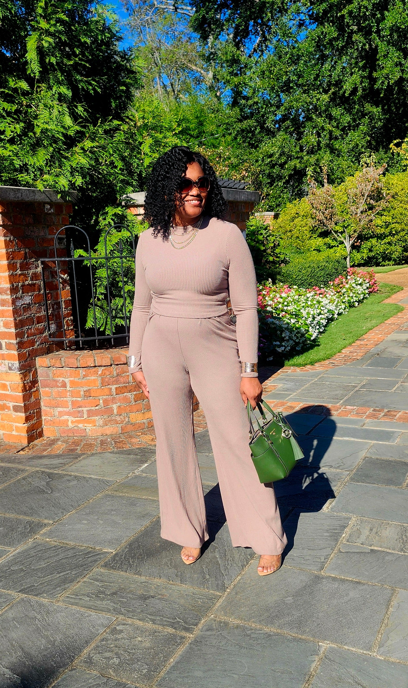 Woman in a beige outfit standing on a stone path with greenery in the background
