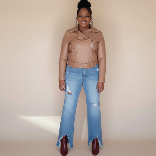 Woman wearing a brown leather jacket and light blue jeans against a beige background